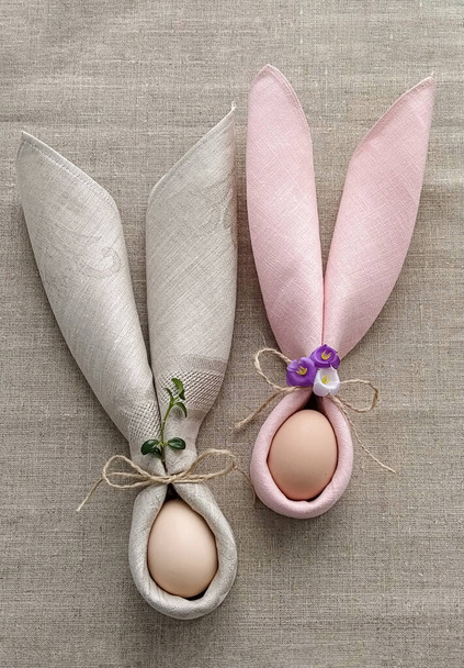 Twee decoratieve konijnenoren van servet met ei op natuurlijke katoenen tafelkleed om Pasen te vieren, doe-het-zelf, plat gelegd - Foto, afbeelding