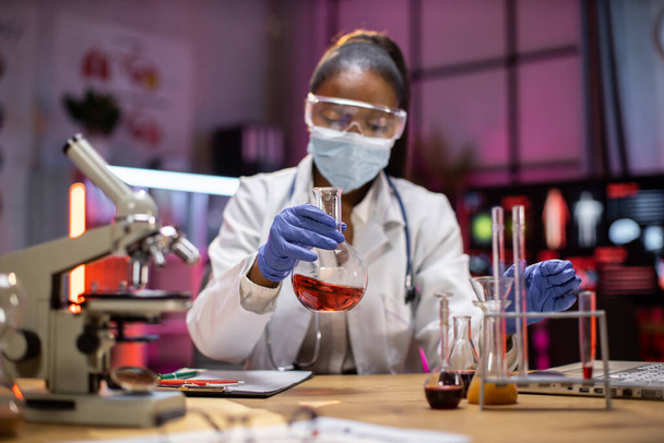 Young scientist african american woman lab technical service holding flask with lab glassware and test tubes in chemical laboratory background, science laboratory research and development medicines. - Foto, Bild
