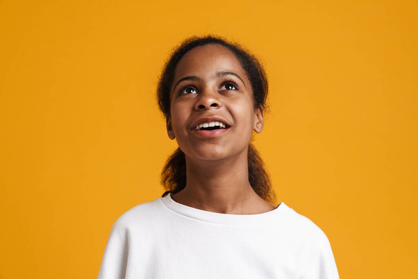 Brunette black girl wearing long-sleeve smiling and looking upward isolated over yellow background - Foto, afbeelding