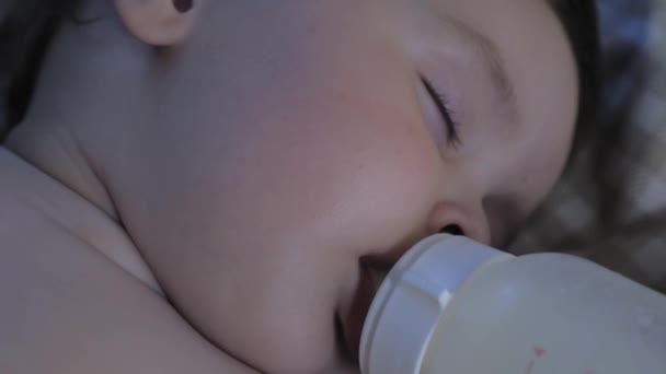 Portrait of a sleeping little child with a bottle in his mouth. The baby eats in a dream. The baby drinks milk from a bottle and sleeps. High quality 4k footage - Materiał filmowy, wideo