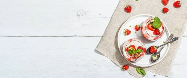 Italian dessert panna cotta in glass with strawberries. Healthy sweet food, trendy hard light, dark shadow. Rustic style concept, white wooden boards background, banner format - Foto, afbeelding