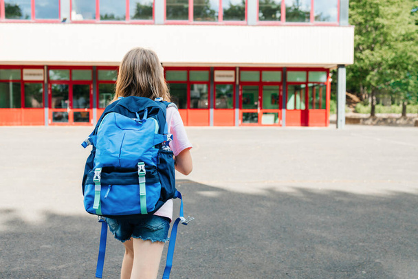 Back view of a schoolgirl with a school backpack on her back going to school. Children are excited about the beginning of the school year and are happy to go to classes. End of vacation. - 写真・画像