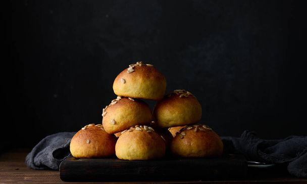 Baked round buns on a wooden table, black background - Photo, Image