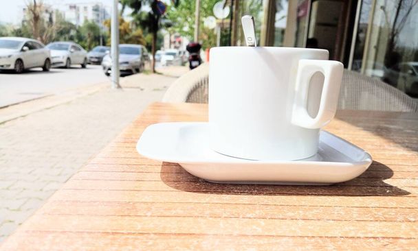Coffee in white cup on the table of the cafe. There are cars parked on the road. Delicious cup of drink. - Foto, immagini