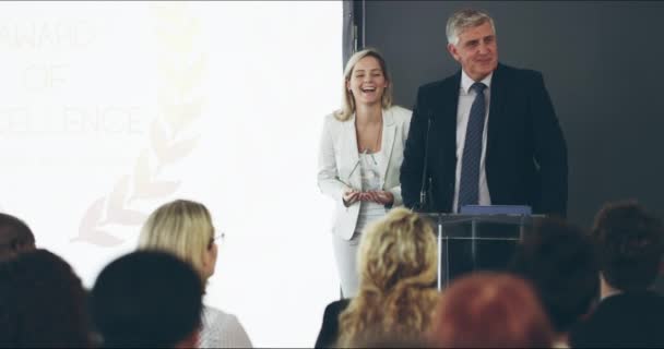 Cheerful businessman delivering a speech during an award ceremony at a corporate business conference. Mature male Ceo and his assistant presenting prizes at a staff year end event. - Filmati, video