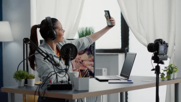 Internet star streaming while sitting at home studio desk and taking selfie photo. Social media influencer sitting in living room while taking pictures with modern touchscreen cellphone. - Filmmaterial, Video