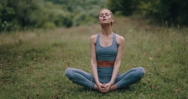 Eine Frau sitzt in Lotus-Pose auf dem Rasen im Park, um zu meditieren und ihren Körper zu strecken. Harmonie mit der Natur und dem Körper als Lebensstil. Hochwertiges 4k Filmmaterial - Filmmaterial, Video