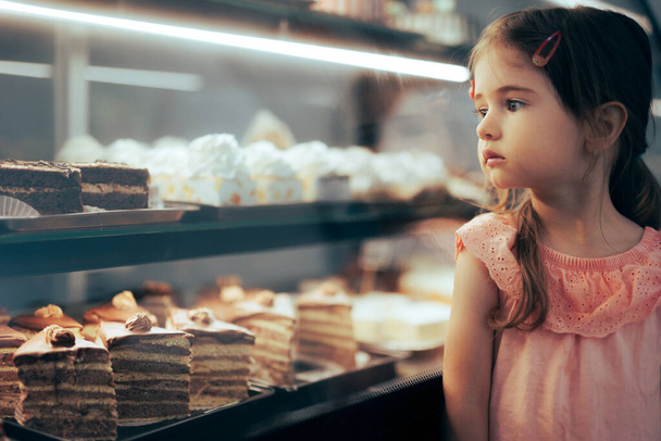 Little Girl Checking Desserts in a Showcase Window of a Confectionery Shop - Fotó, kép
