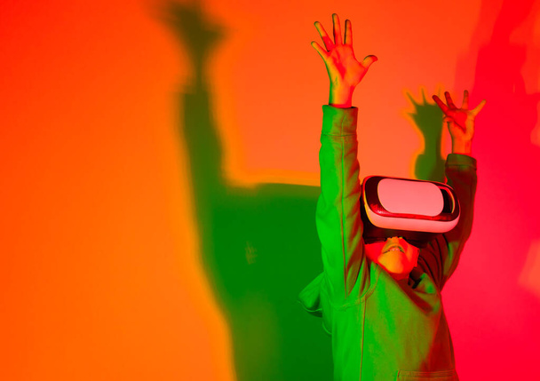 6-7 year old boy with his hands up playing with virtual reality glasses in front of a colorful lights background. High quality photo - 写真・画像