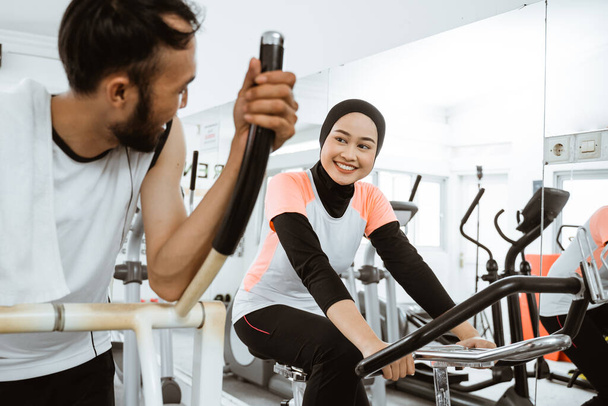 two beautiful woman with hijab and friend at the gym exercising with friend on static elliptical cycle machine together - 写真・画像
