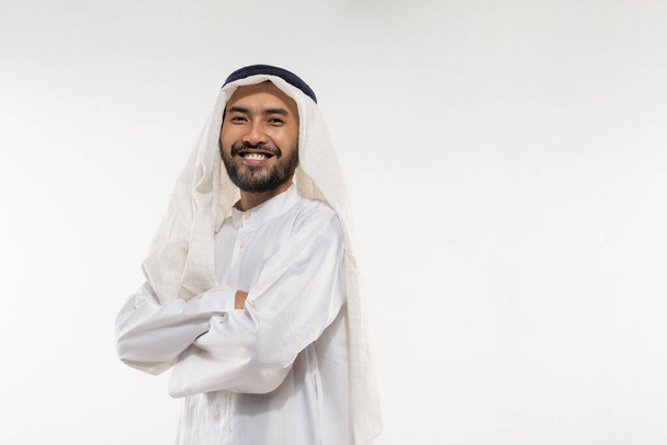 an arabian young man in a turban standing smiling with crossed hands on a plain background - 写真・画像