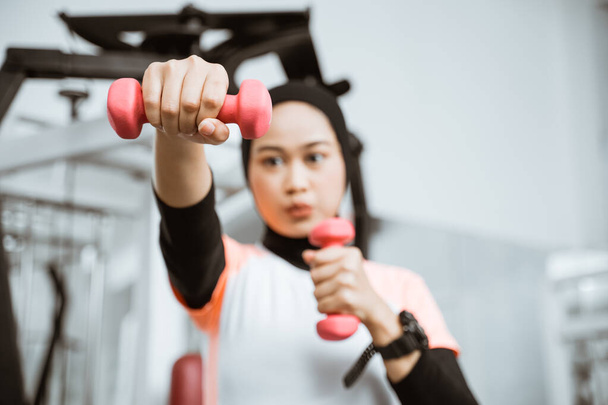 Asian muslim woman doing exercise, lifting dumbbell at the gym - Foto, Imagem