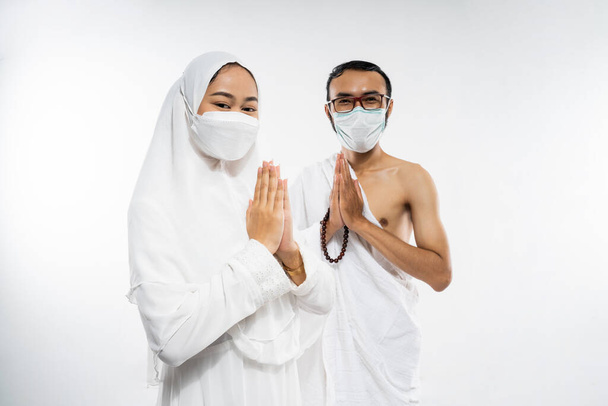 Asian couple wearing ihram clothes and mask with salam gesture on isolated background - Foto, imagen