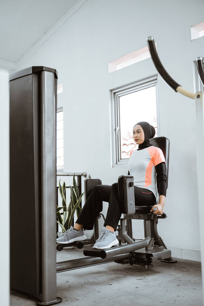 muslim asian woman working on her lower body using leg machine at the gym - Foto, Bild