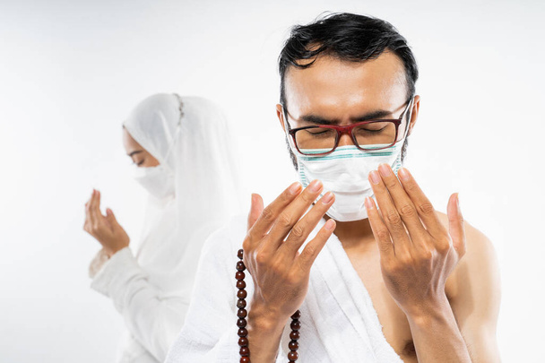 Man wearing ihram clothes and mask performing al fatihah prayer on isolated background - Фото, зображення