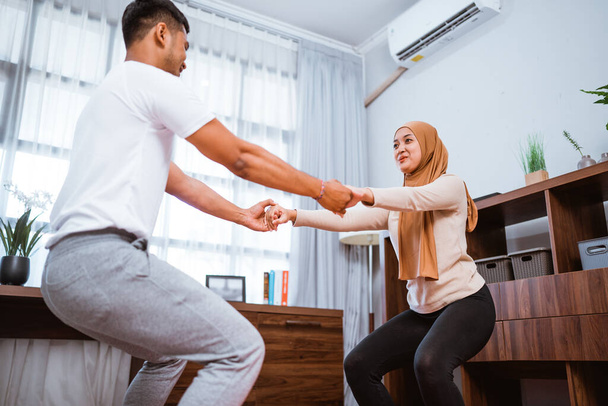muslim couple exercising doing squat together facing each other at home - Zdjęcie, obraz