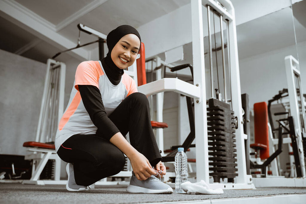 beautiful muslim girl tying shoelaces on sports shoes in gym - Фото, зображення