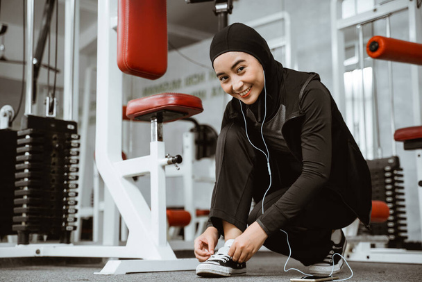 beautiful muslim girl tying shoelaces on sports shoes in gym - Zdjęcie, obraz