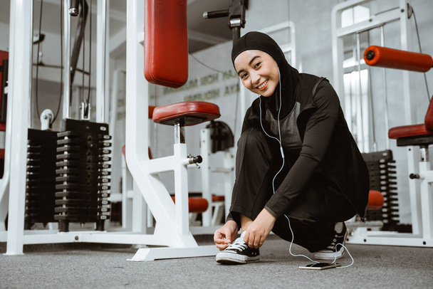 beautiful muslim girl tying shoelaces on sports shoes in gym - Foto, Imagem
