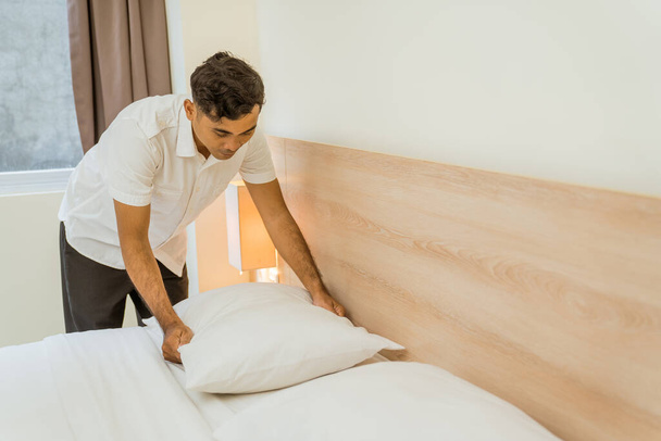 Asian male cleaning staff tidying pillows on bed in hotel room - Φωτογραφία, εικόνα