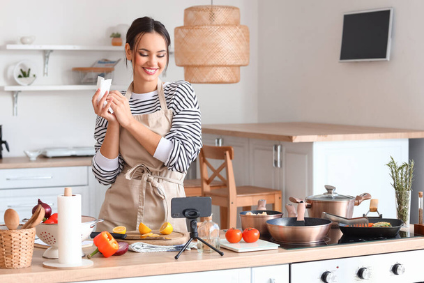 Young woman wiping her hands with paper towel while watching cooking video tutorial in kitchen - Foto, Bild