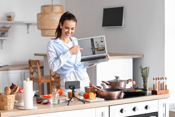 Young woman with laptop recording cooking video tutorial in kitchen - Photo, Image