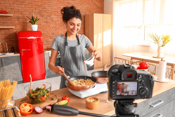Young woman pouring pasta with sauce while recording video class in kitchen - Φωτογραφία, εικόνα