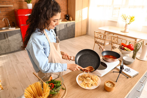 Young woman putting pasta onto plate while recording video class in kitchen - Foto, Imagen