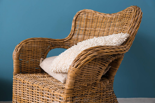 Rattan armchair with pillow near blue wall - Фото, изображение