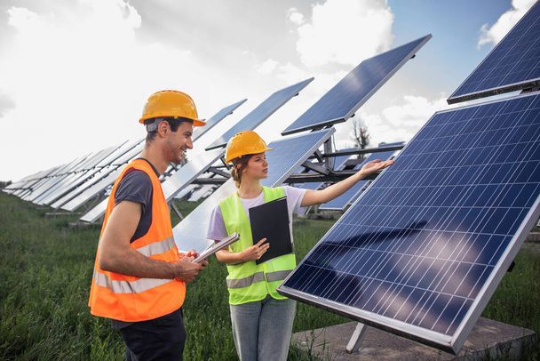 Two technician lady and man analysing together and discussing about cleanliness of photovoltaic solar panels they standing in the middle of solar power farm. - Фото, зображення