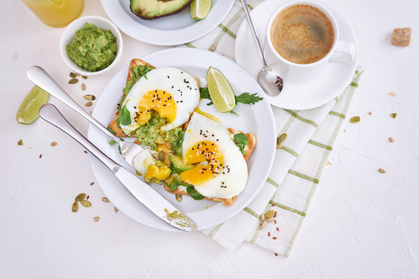 healthy breakfast or snack - sliced avocado and fried egg on toasted bread and cup of coffee. - Фото, изображение