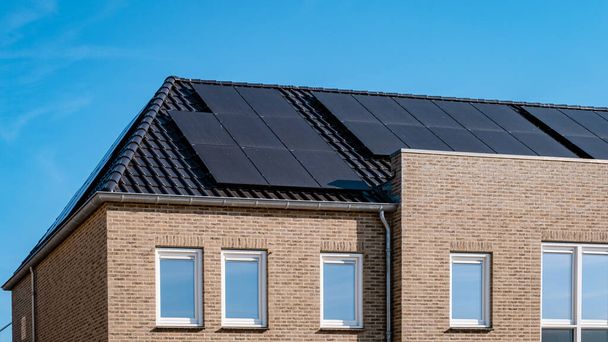 Newly build houses with solar panels attached on the roof against a sunny sky Close up of a new building with black solar panels. Zonnepanelen, Zonne energie, Translation: Solar panel, , Sun Energy.  - Photo, Image