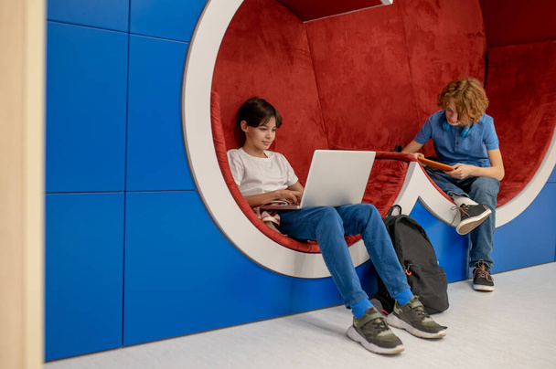 Doing homework. Two school boys feeling comfortable in the lounge zone and doing homework - Foto, Bild