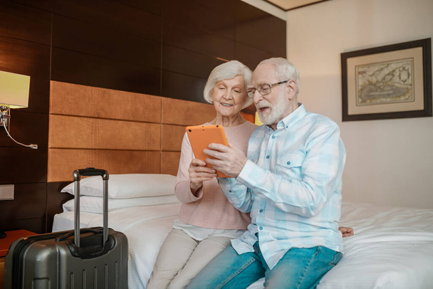 On internet. Senior couple sitting on a bed and watching something on a talet - Foto, imagen