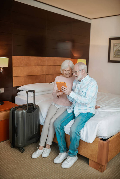 On internet. Senior couple sitting on a bed and watching something on a talet - Foto, imagen