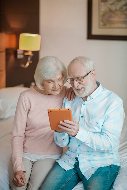 On internet. Senior couple sitting on a bed and watching something on a talet - Fotoğraf, Görsel
