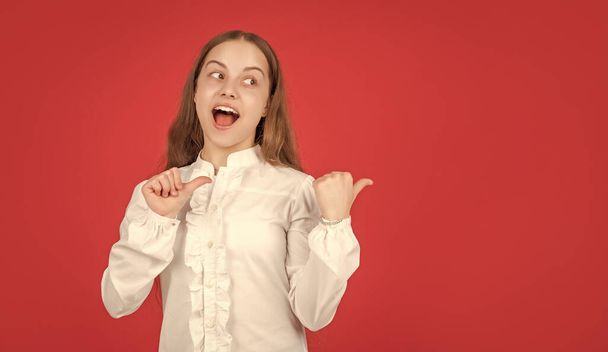 surprised teen girl in white shirt pointing finger on red background copy space, directing. - Fotografie, Obrázek