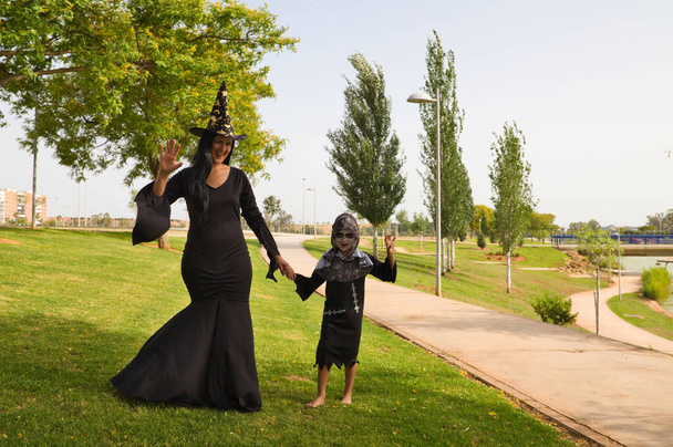 Щасливого Хеллоуїна. Дитина, одягнена на вечірку на Хеллоуїн і його мати, одягнена як відьма, що йде в парку. Трюк або частування
. - Фото, зображення