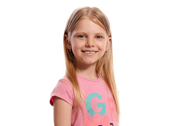 Close-up portrait of a cheerful blonde kid with a long hair, in a pink t-shirt, looking at the camera isolated on white background with copy space. Concept of a joyful childhood. - Фото, зображення