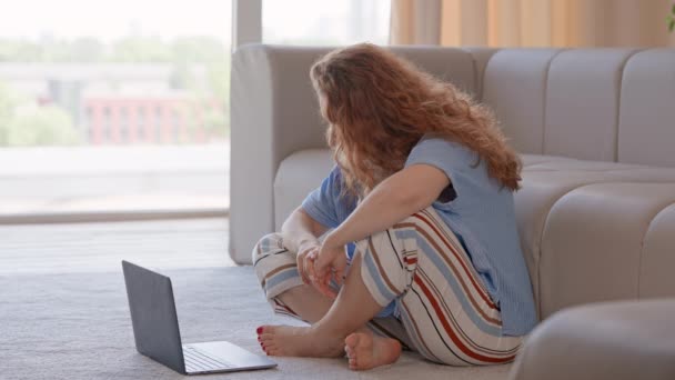 middle aged woman sitting on the floor with crossed legs watching online yoga or meditation class on laptop meditating in apartment morning routine for calmness - Metraje, vídeo