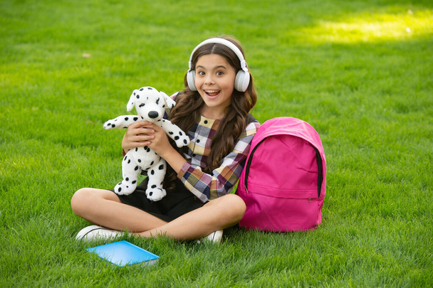 Surprised teenage girl listening to music holding dog toy on grass after school, education. back to school. pupil at school time. - Photo, image