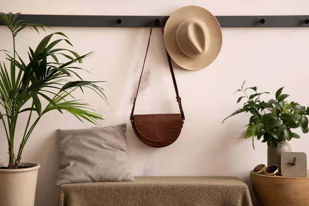 The stylish composition of cosy entryway with hanger, bench with green plaid and pillow, plants and personal accessories. Beige wall. Home decor. Template.  - 写真・画像