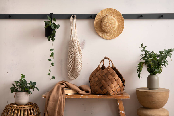 The stylish composition of cosy entryway with wooden bench, coffee table, basket, hanger and personal accessories. Beige wall. Home decor. Template.  - 写真・画像
