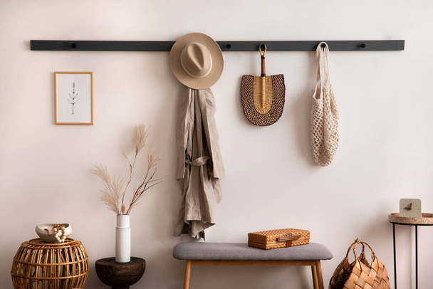 The stylish composition of cosy entryway with wooden basket, carpet, hanger and personal accessories. Beige wall. Home decor. Template.  - Фото, изображение