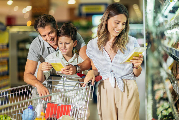 Happy family with child and shopping cart buying food at grocery store or supermarket - Foto, Bild