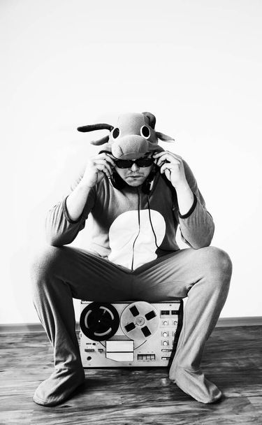 Hombre disfrazado de cosplay de una vaca con grabadora de carrete. Un tipo con pijamas de animales. Foto divertida con ideas de fiesta. Disco música retro. - Foto, imagen