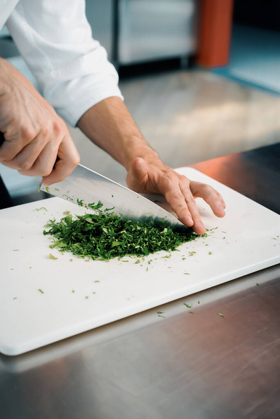 Close-up of a chef finely chopping herbs in a professional kitchen - Foto, afbeelding