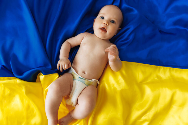 Pray for Ukraine A smiling little girl lies on the Ukrainian Blue and Yellow flag. The child gives hope for the best. protest against war, peace, end of aggression, child against Russian war - 写真・画像