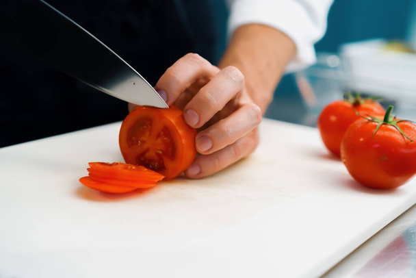 Close-up of chef slicing tomato in a professional restaurant kitchen - Foto, Imagen