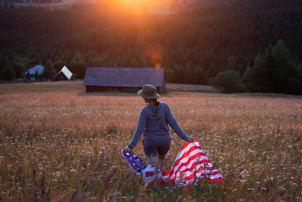 Young woman holding american USA flag in the sunset. Independence Day or traveling in America concept.  - Foto, afbeelding